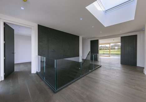 Modern hallway with glass balustrade staircase, skylight, and large sliding doors opening to countryside views.